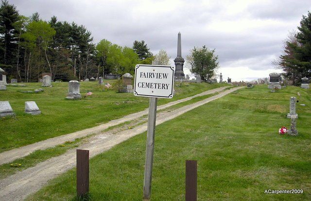 Rural cemetery entrance with sign along a dirt road under cloudy skies