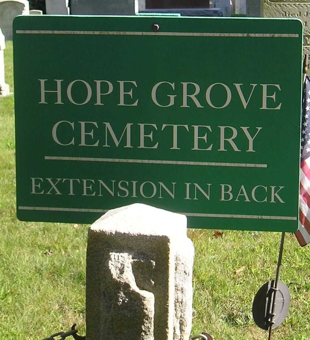 Green sign reading “Hope Grove Cemetery Extension in Back” with a stone post and grass background