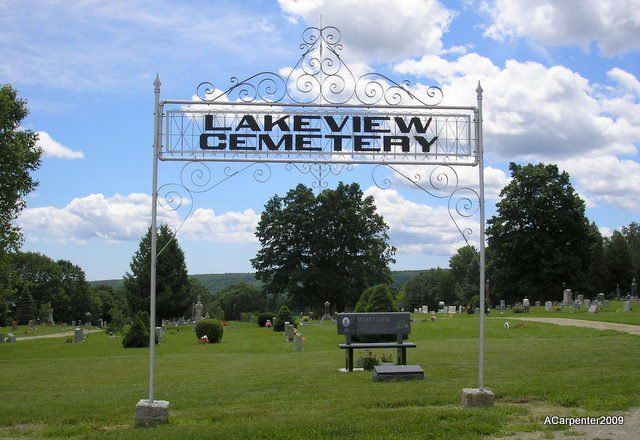 Lakeview Cemetery sign over a grassy cemetery with trees, benches, and headstones under a blue sky