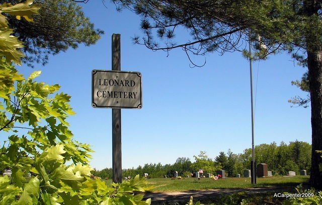 Sign for an old cemetery beside a grassy park under a blue sky, framed by trees