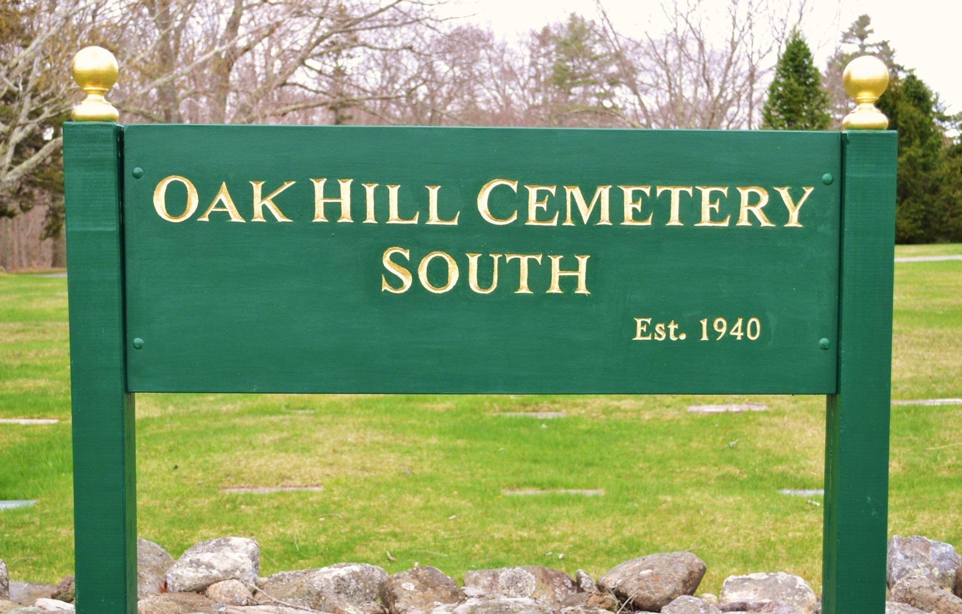 Green sign reading “Oak Hill Cemetery South” with “Est. 1940” in a grassy outdoor setting