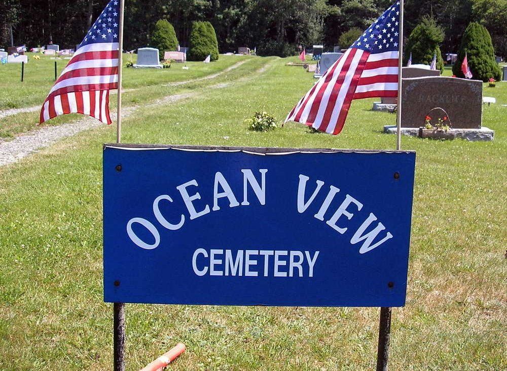 Blue Ocean View Cemetery sign with American flags in a grassy cemetery