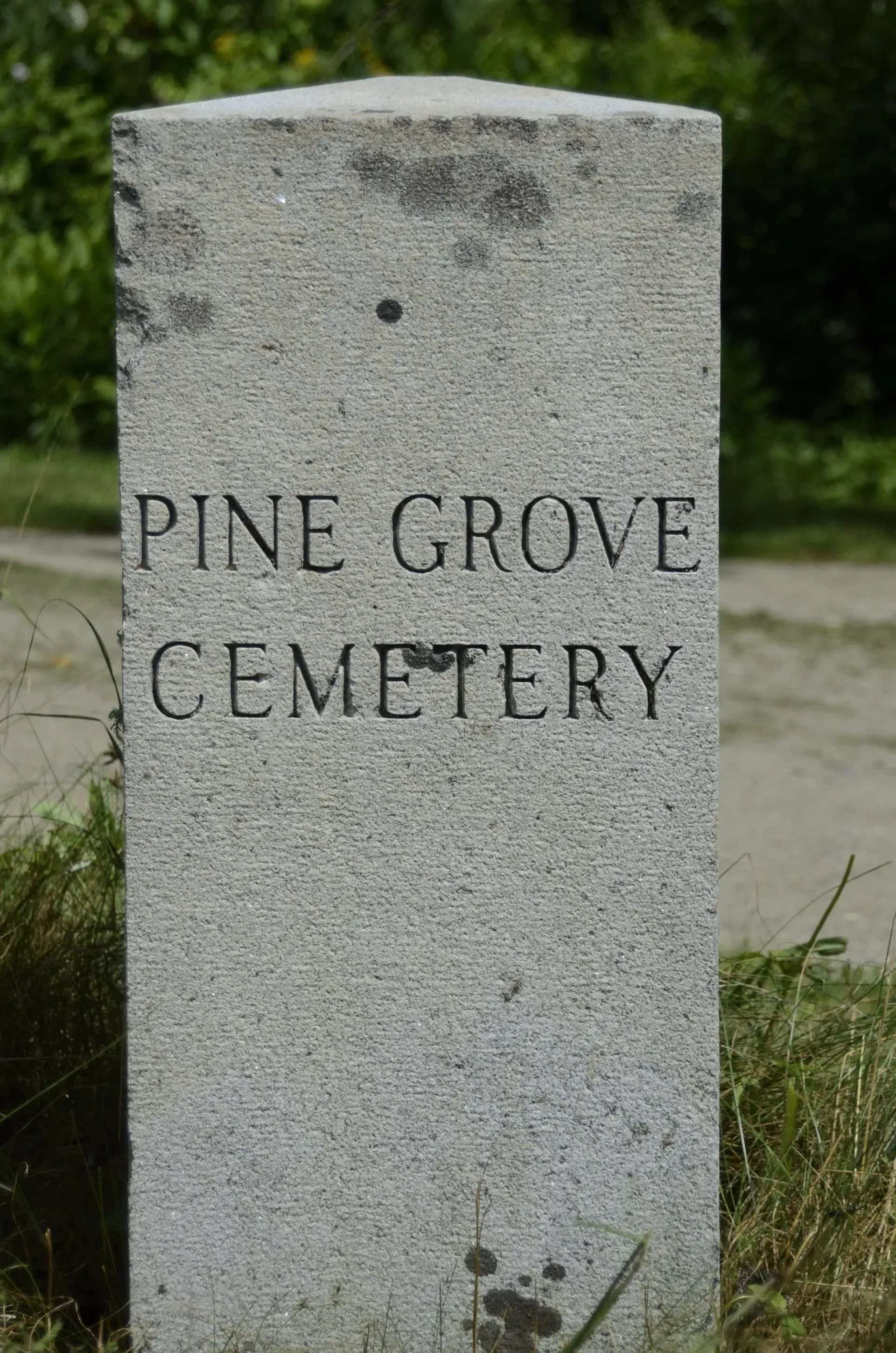 Gray stone cemetery marker reading “PINE GROVE CEMETERY” outdoors.