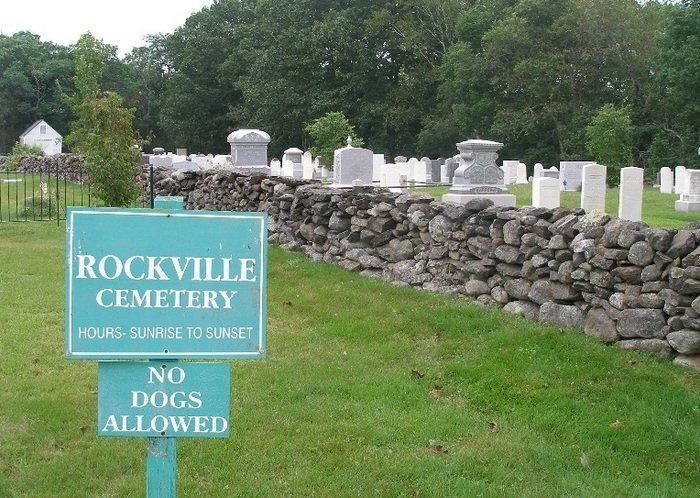 Rockville Cemetery sign beside stone wall and gravestones, with a no dogs allowed notice.