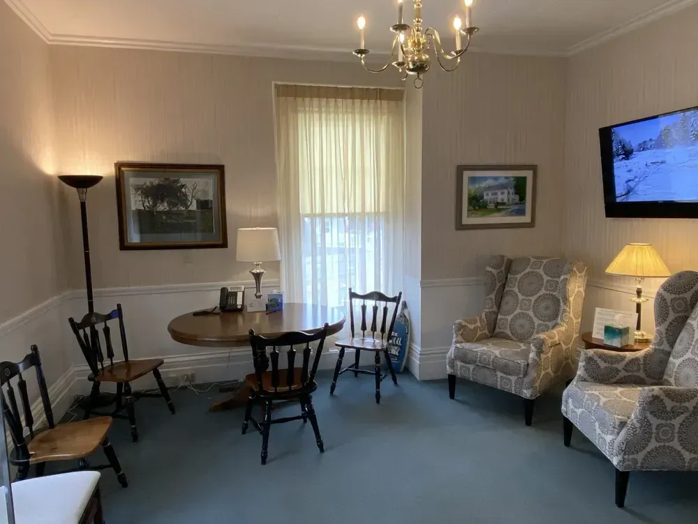 Cozy living room with chairs around a table, floral armchairs, lamp, chandelier, and wall-mounted TV