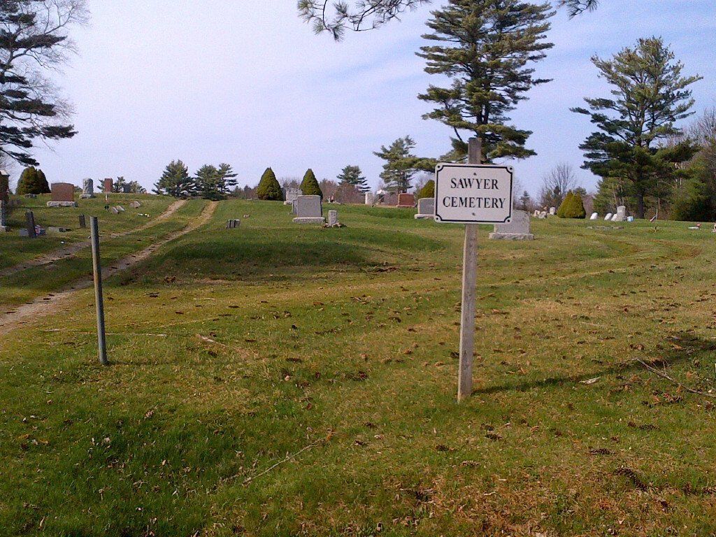 Grassy cemetery hill with headstones and a sign reading “South Cemetery” under cloudy skies