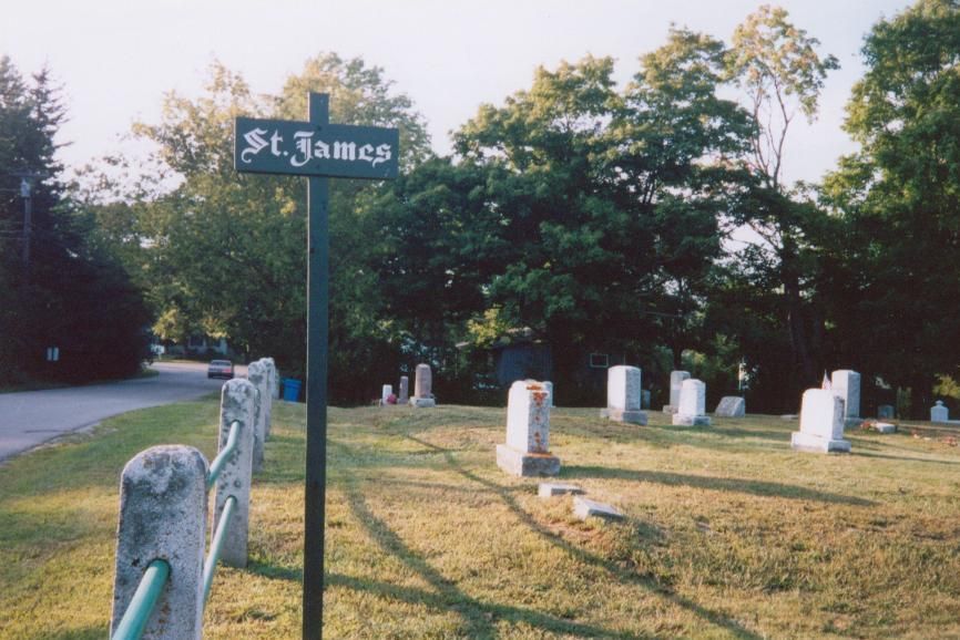 St. James cemetery sign beside a row of white headstones in a grassy, tree-lined area