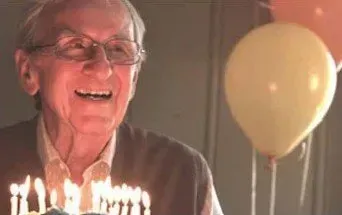 Smiling person beside birthday candles and a yellow balloon indoors