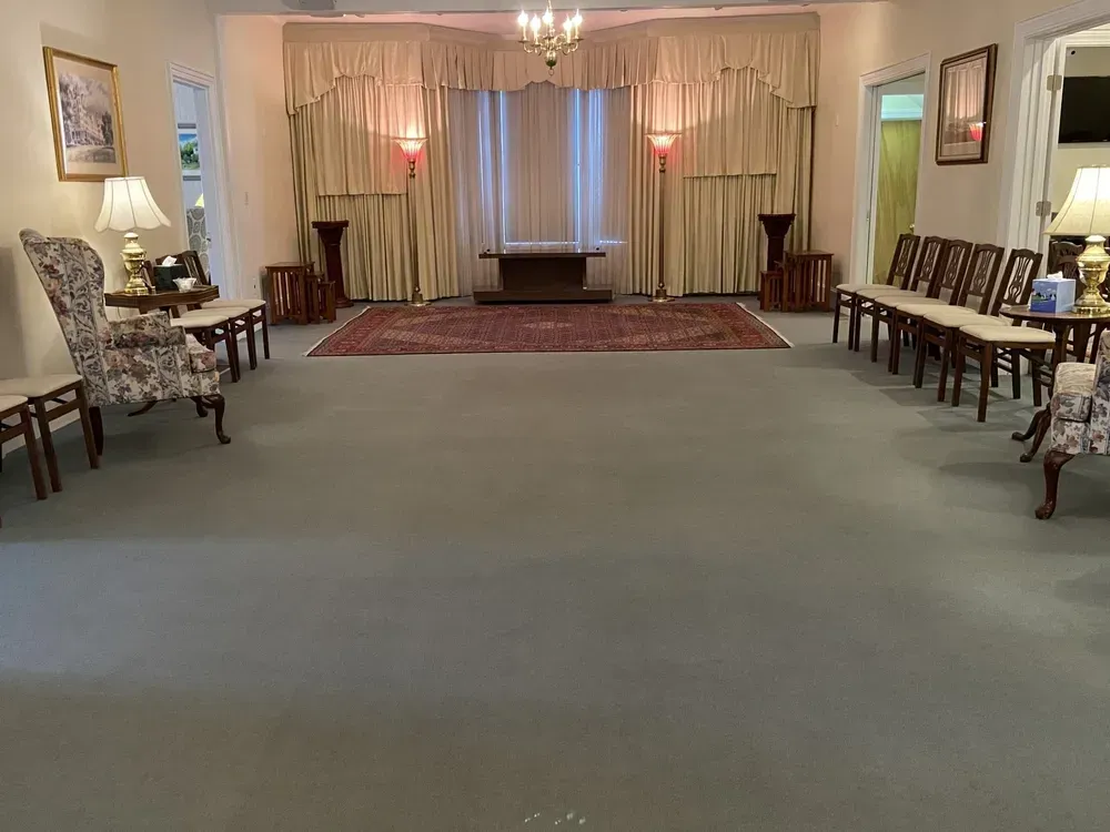 Empty formal room with chairs along both walls, a red rug, and soft curtains around a small stage area