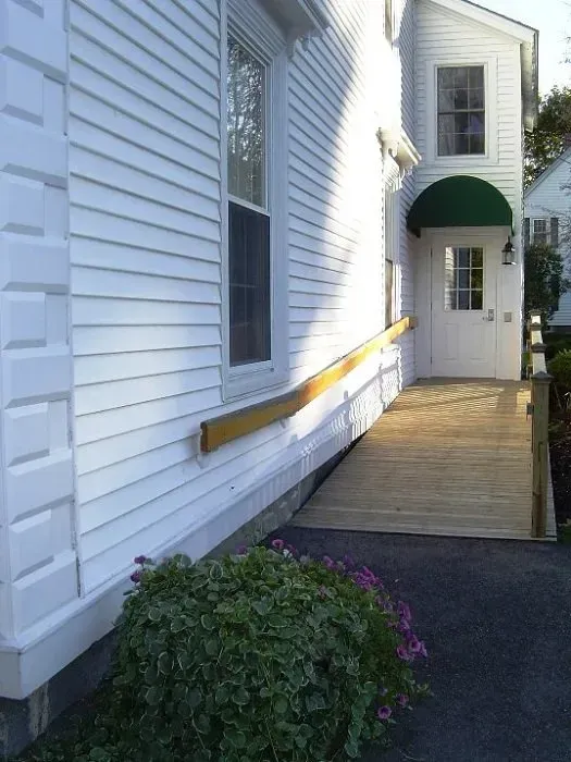 Exterior ramp with yellow handrail leading to a white house entrance under a green awning