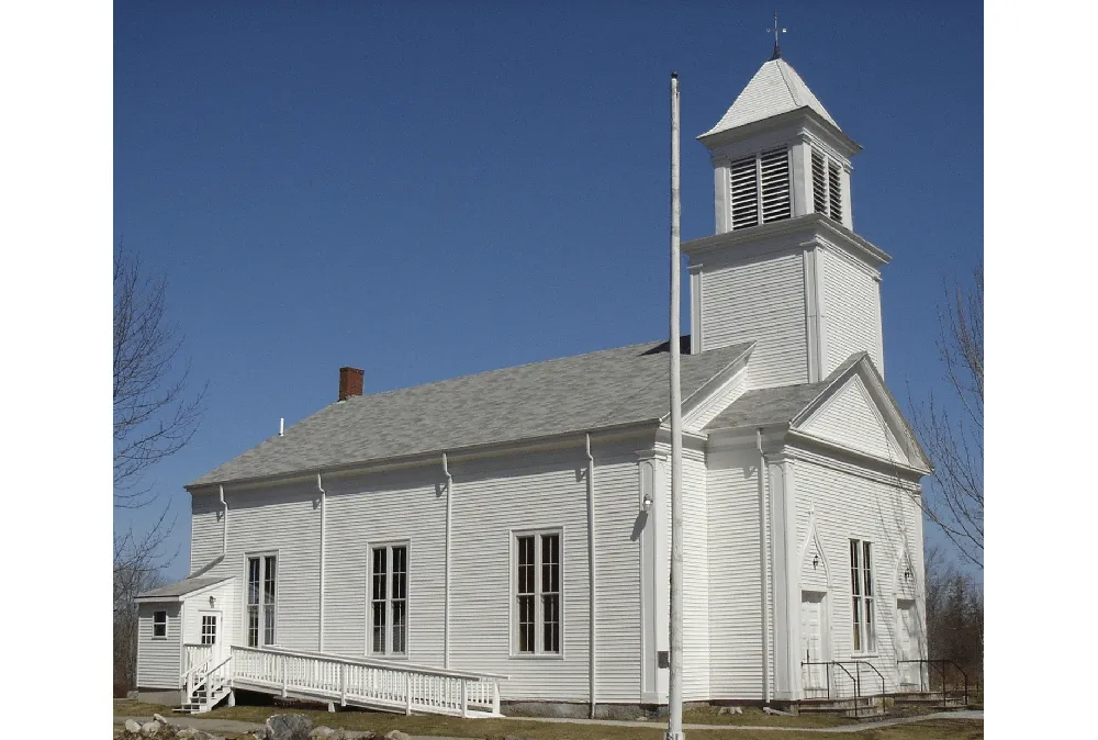 White wooden church with steeple and flagpole under a clear blue sky