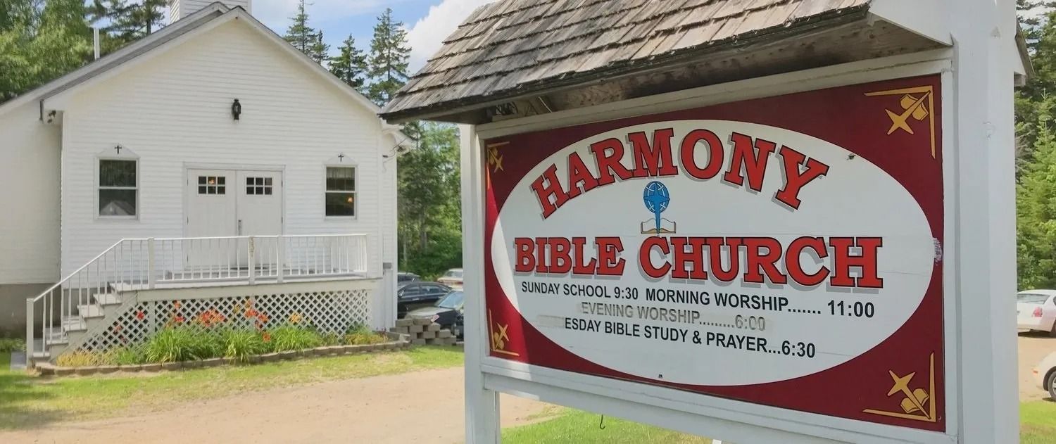 Harmony Bible Church sign beside a white church building with a porch and trees in the background