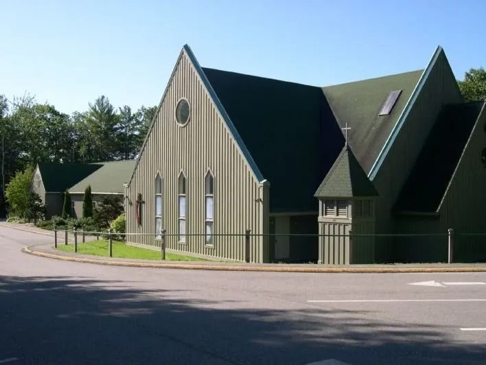 A green-and-tan church with steep gables beside a road on a sunny day