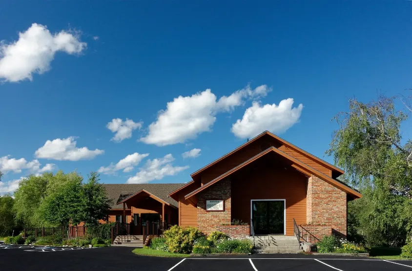 Single-story wooden building with a parking lot under a blue sky with clouds