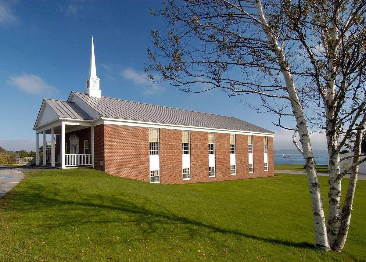 Small brick church with white steeple on a grassy field by the water