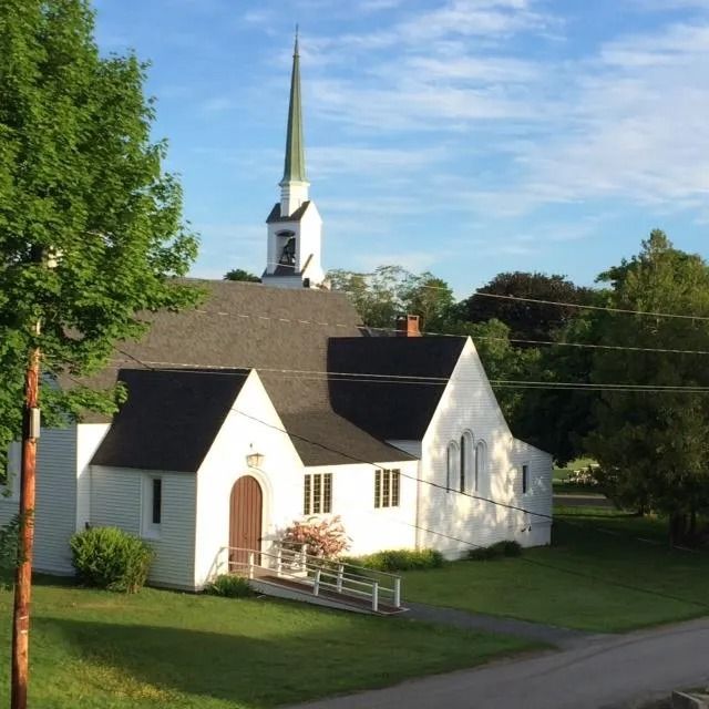 Small white church with steeple on a grassy hill beside a road on a sunny day