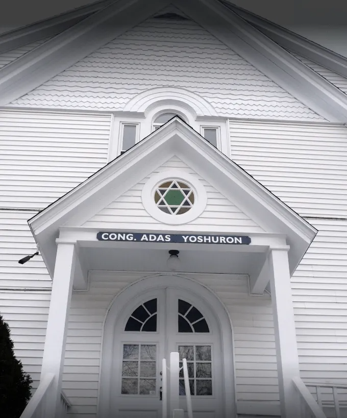 White synagogue entrance with arched doorway and sign reading “Cong. Adas Yeshuron”