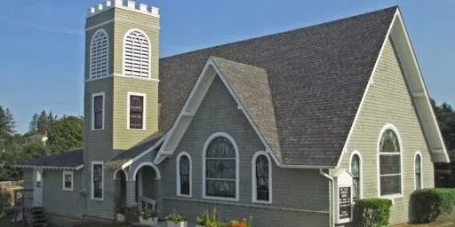 Gray church with arched windows and a tall tower under a blue sky