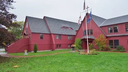 Red barn-style building with a red entrance, green lawn, and flagpoles on an overcast day