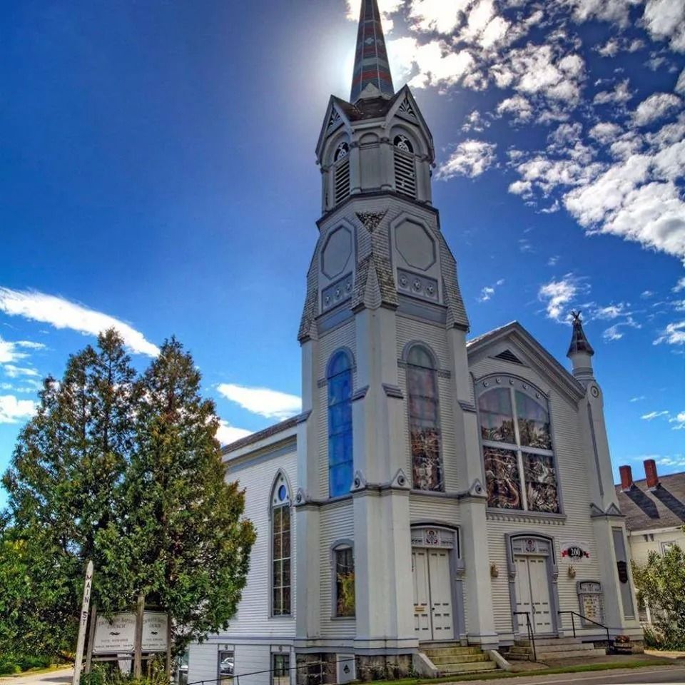 White church with tall steeple on a sunny street under a blue sky with clouds