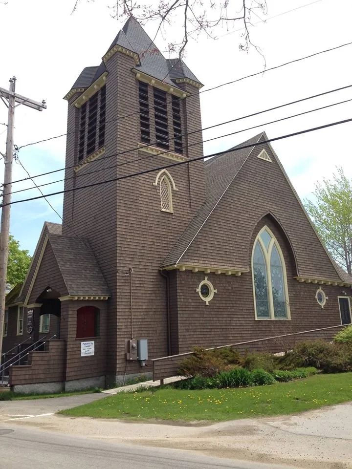 Brown wooden church with a steeple and stained-glass windows on a street corner