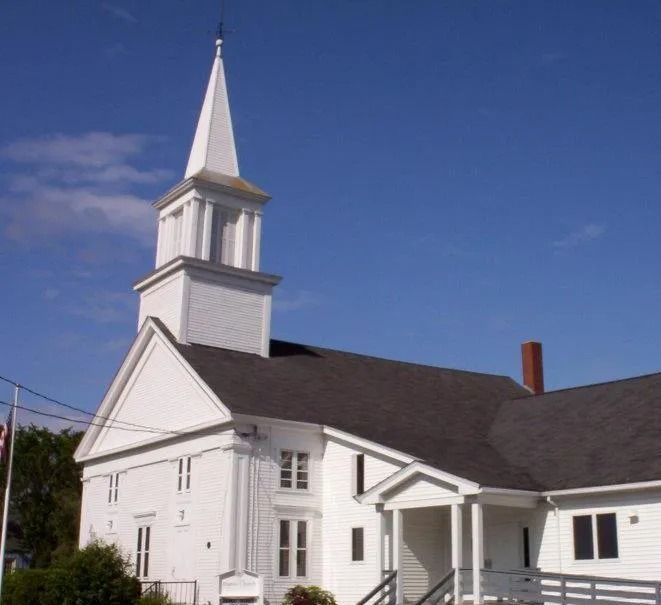 White church with tall steeple and dark roof under a clear blue sky