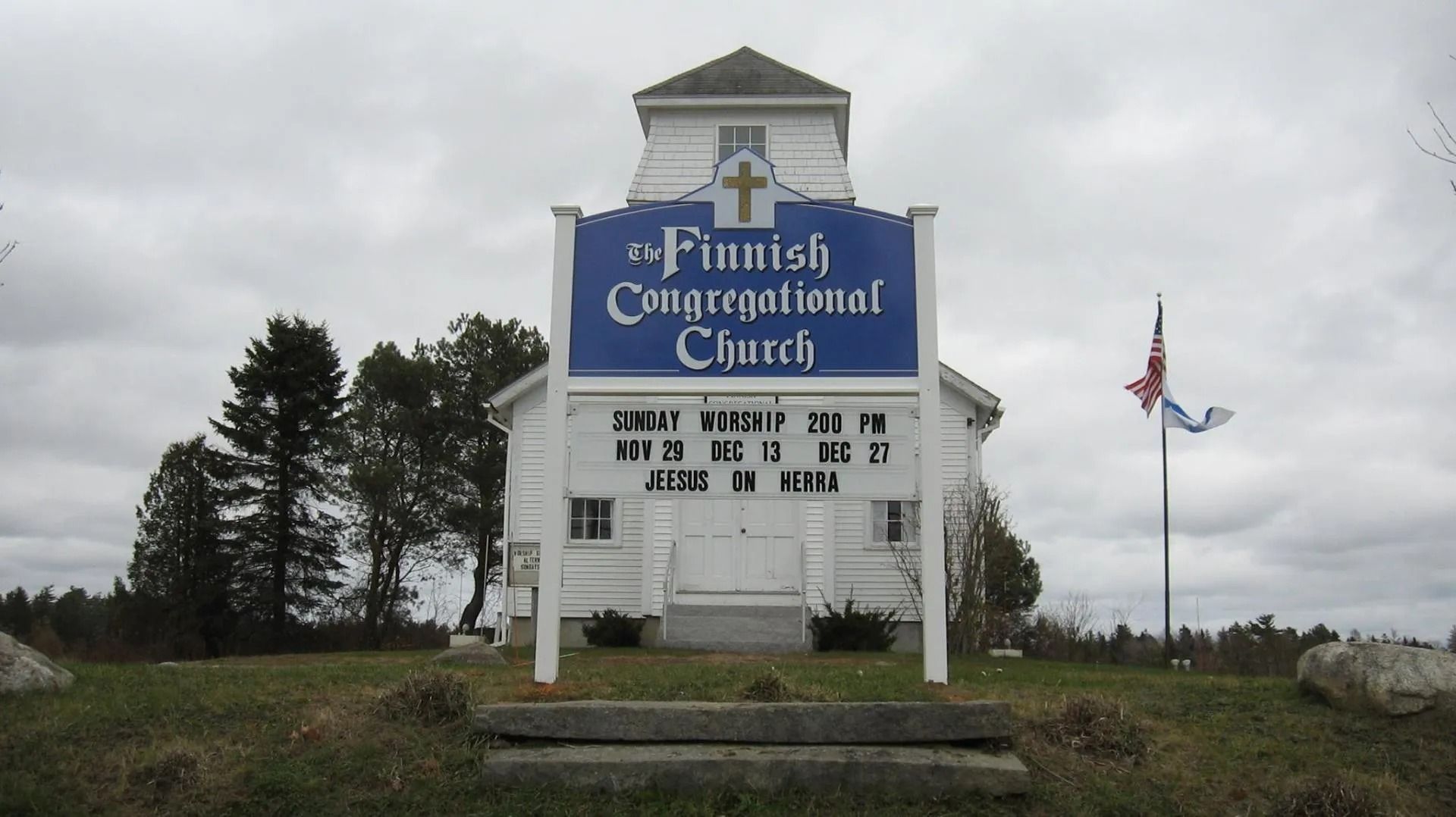 St. Peter’s Congregational Church sign beside a flagpole under a cloudy sky