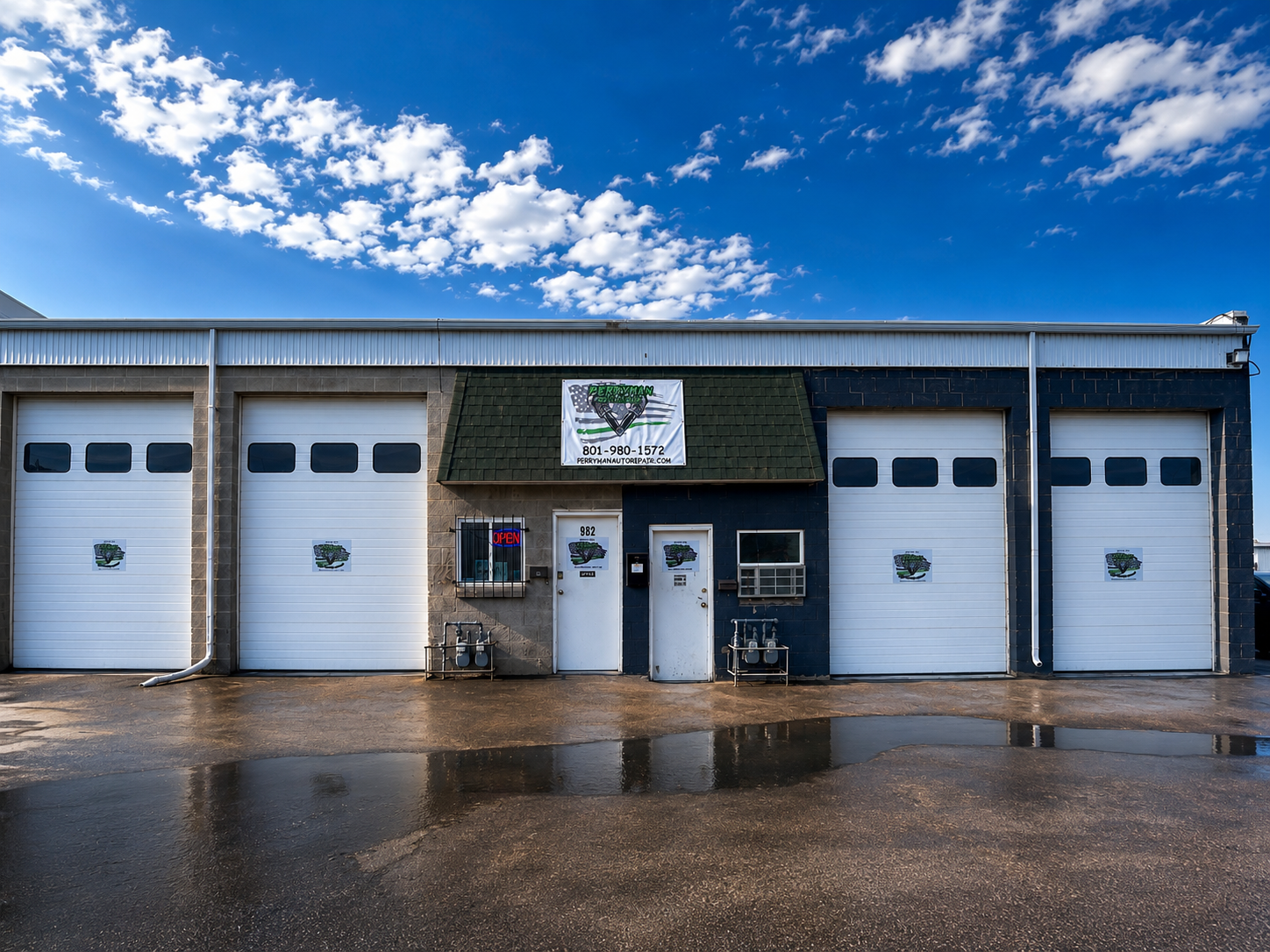 Auto repair shop with four white garage doors under a blue sky, wet pavement in front | Perryman Auto Repair