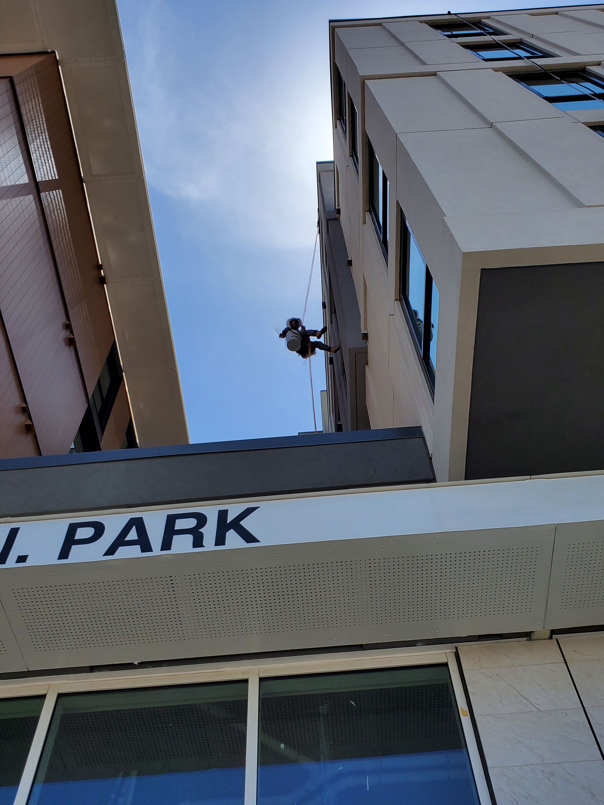 Low-angle view of tall apartment buildings against a blue sky, with a person standing on a ledge.