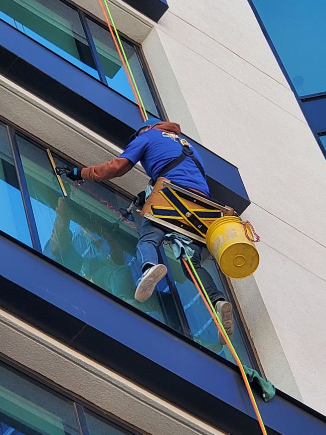 Window cleaner on a suspended harness cleaning a tall building’s glass windows