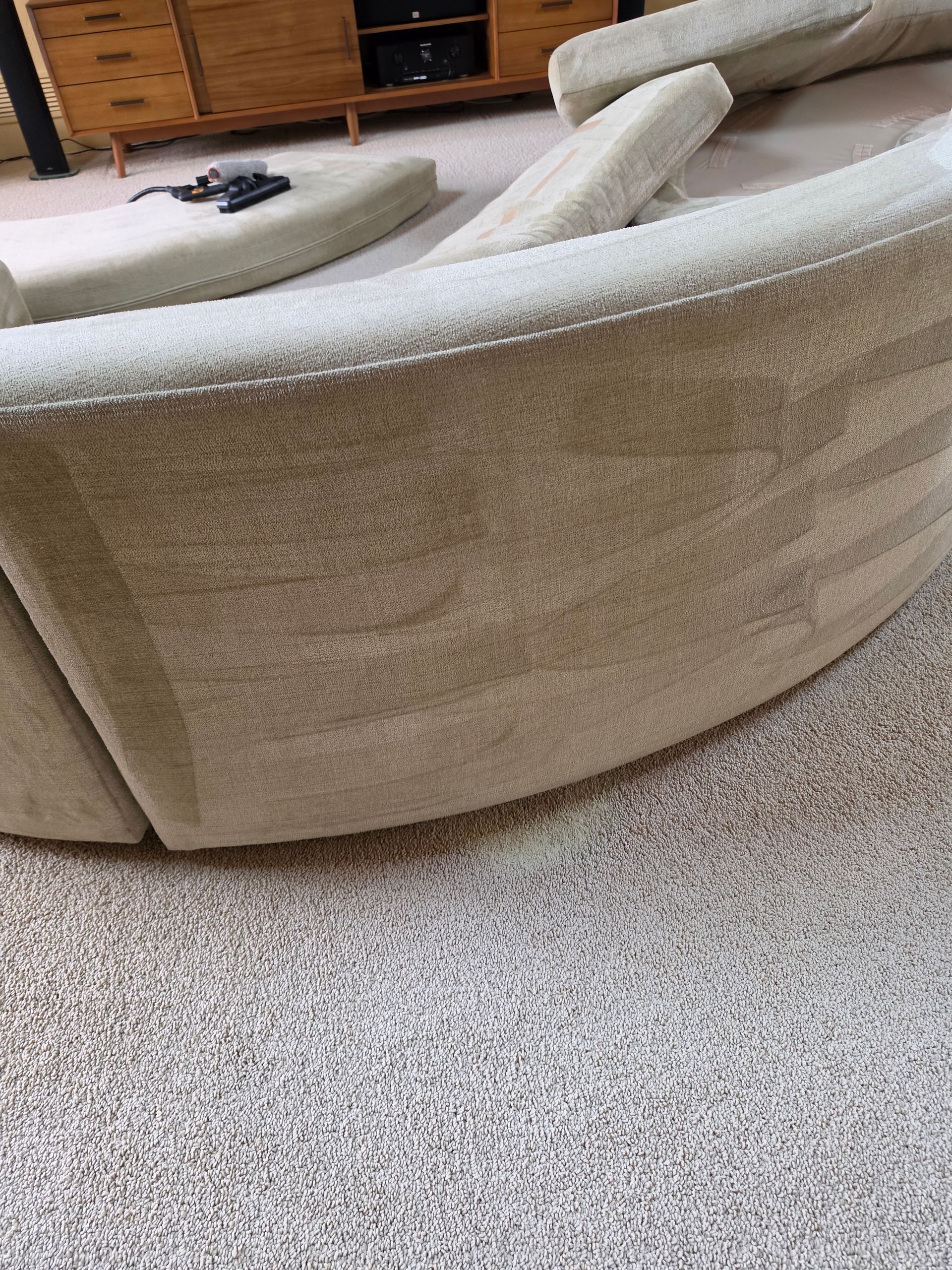 Curved beige sofa with matching round ottoman on speckled carpet in a living room.