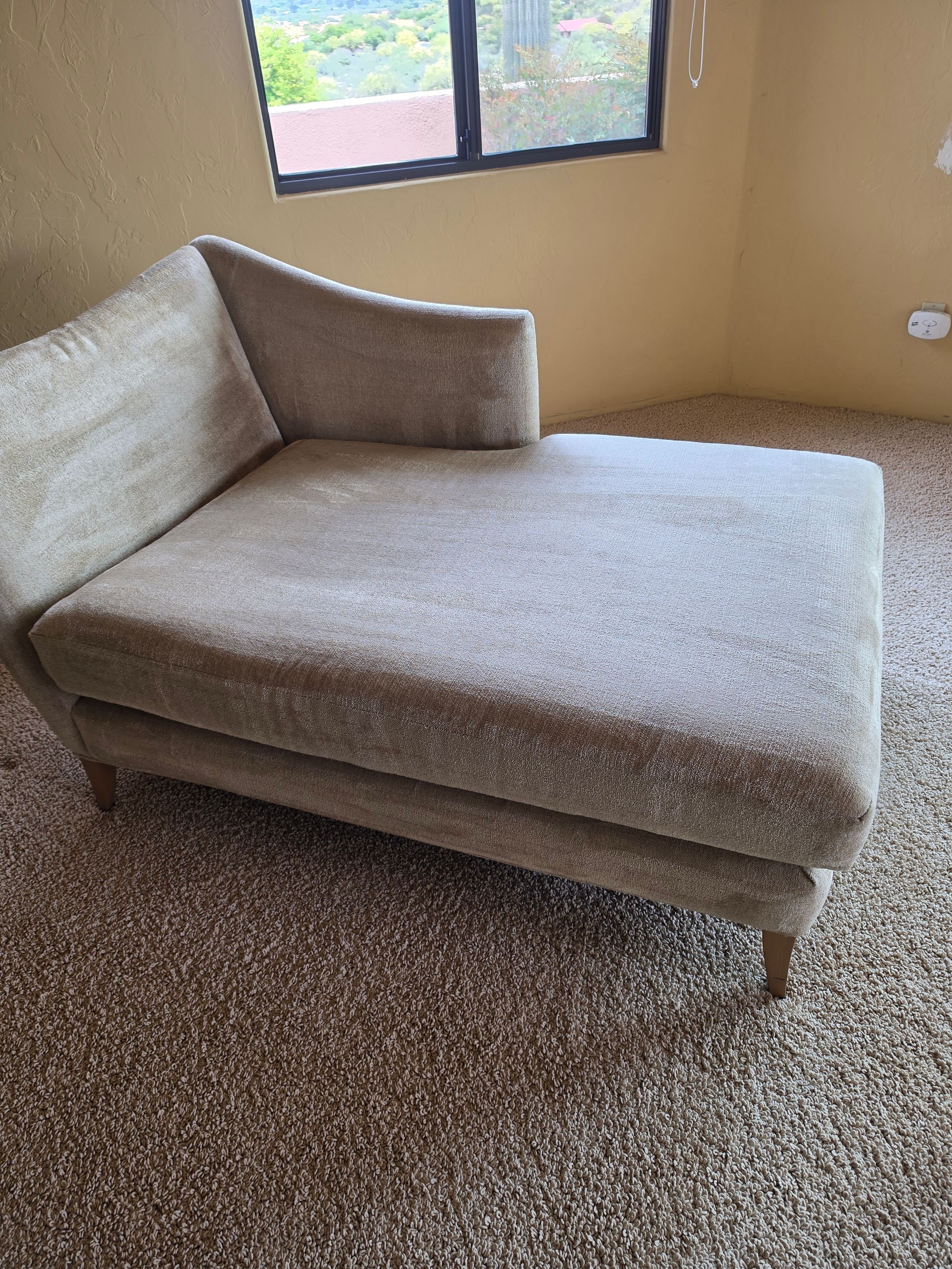 Gray chaise lounge in a carpeted room beside a window.