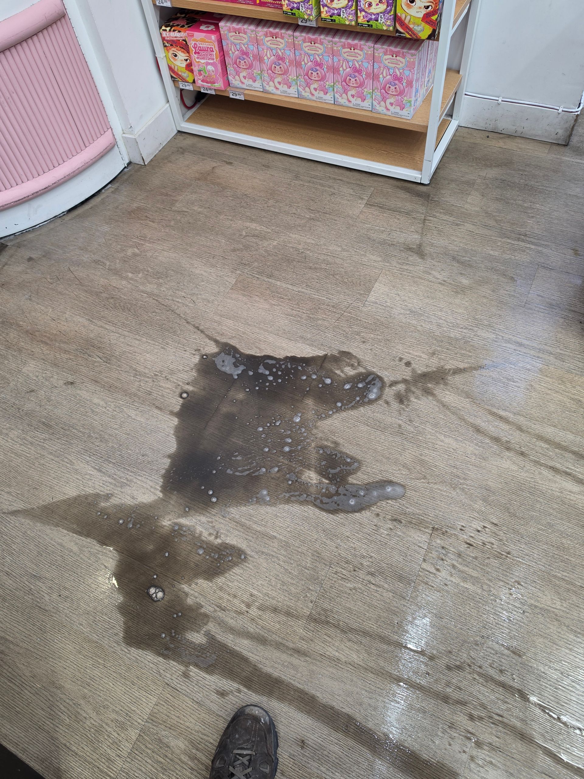 A stained carpet with a large dark spill near a white shelf of colorful folded items.