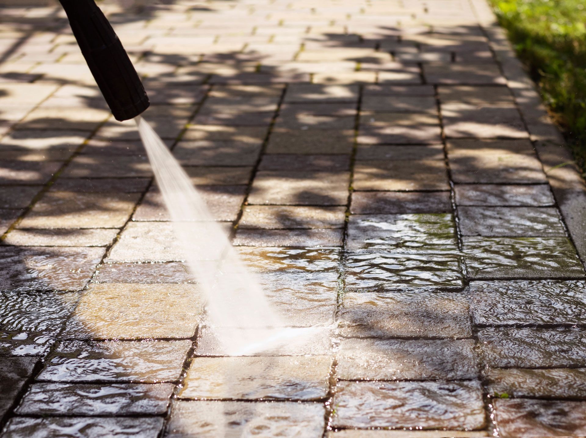 A hose sprays water onto a wet stone patio in sunlight.