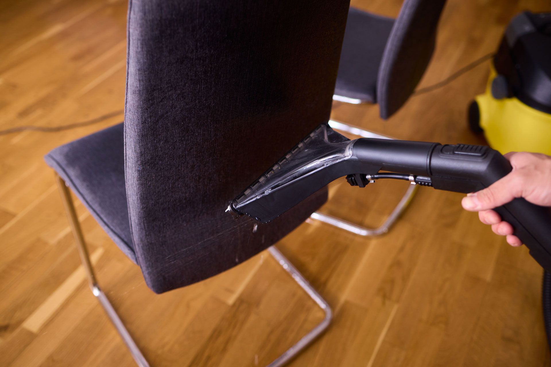 Hand vacuum cleaning a black chair seat on a wooden floor