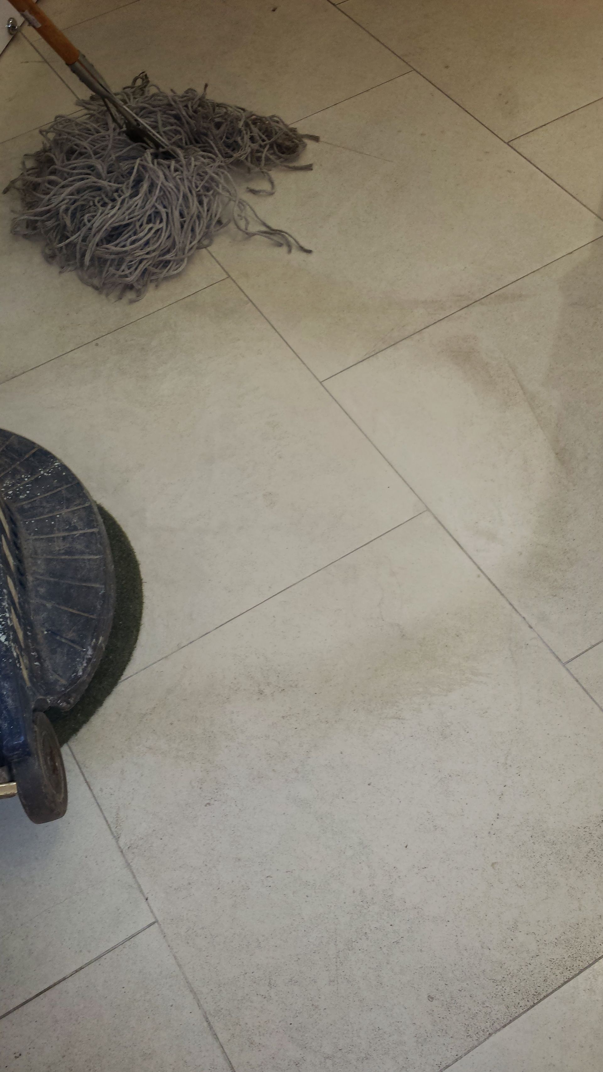 Gray mop on a beige tiled floor beside a dark chair leg