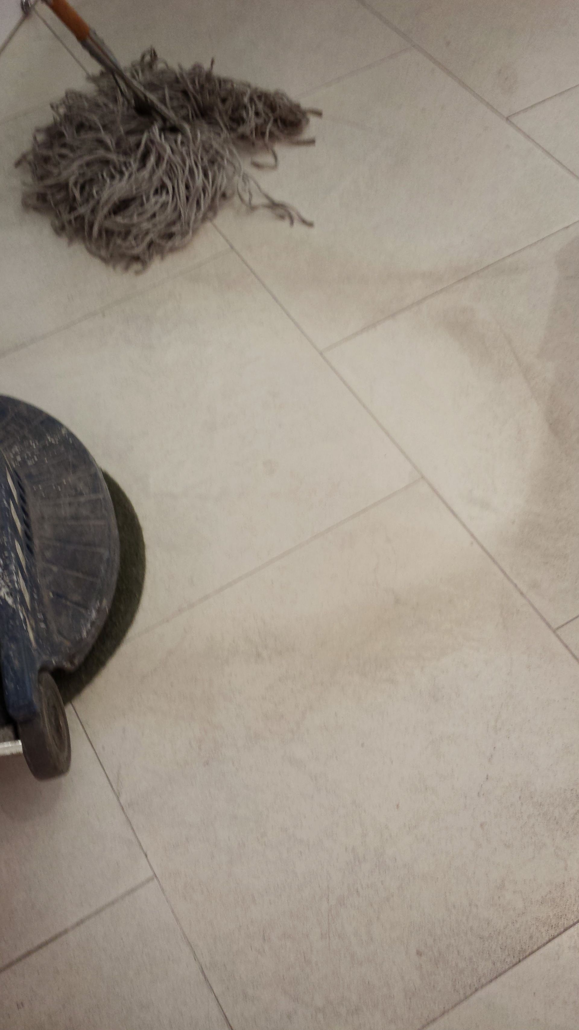 Gray mop lying on a beige tiled floor beside the edge of a black chair leg