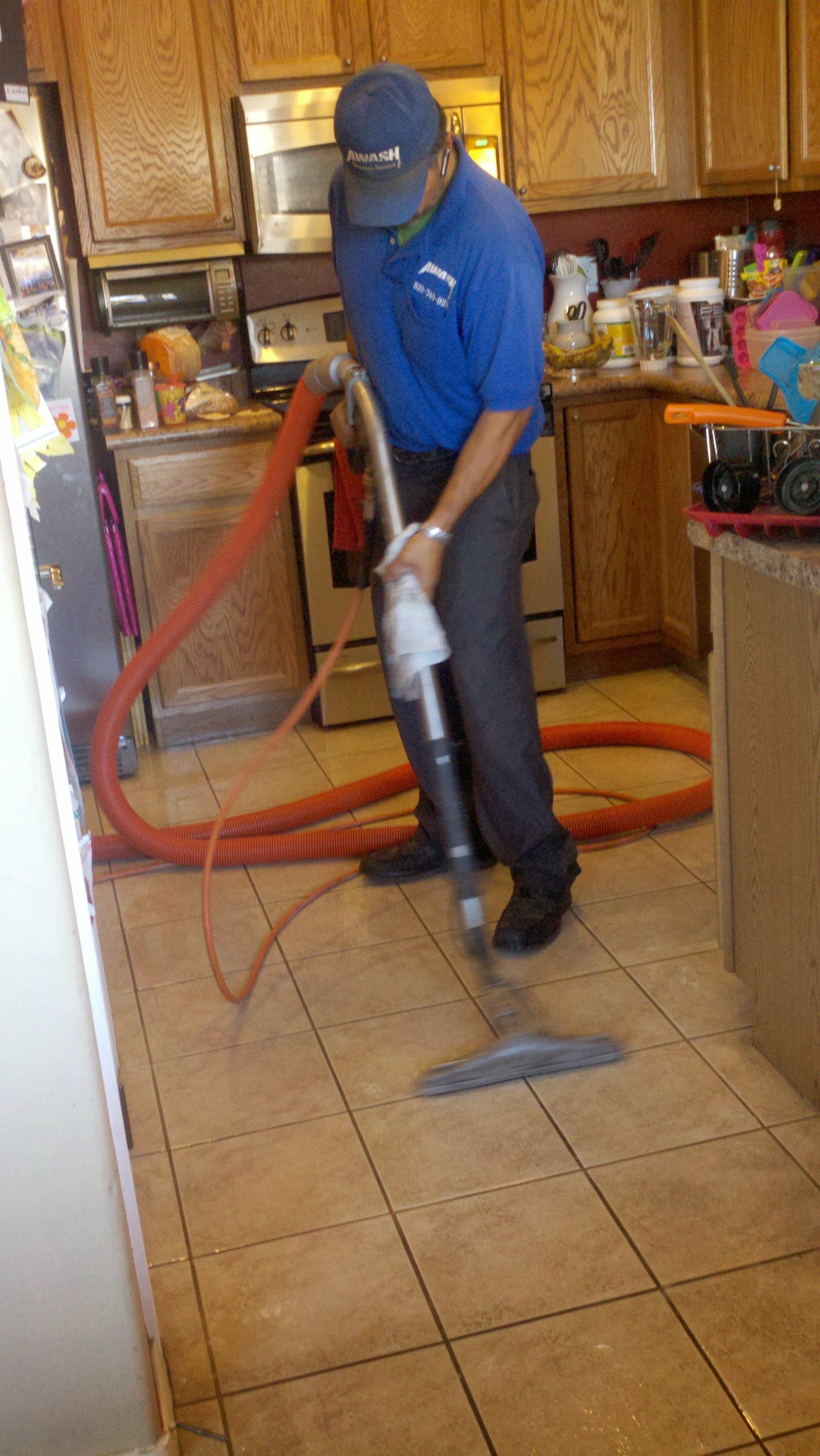 Worker using a vacuum hose to clean a tiled kitchen floor