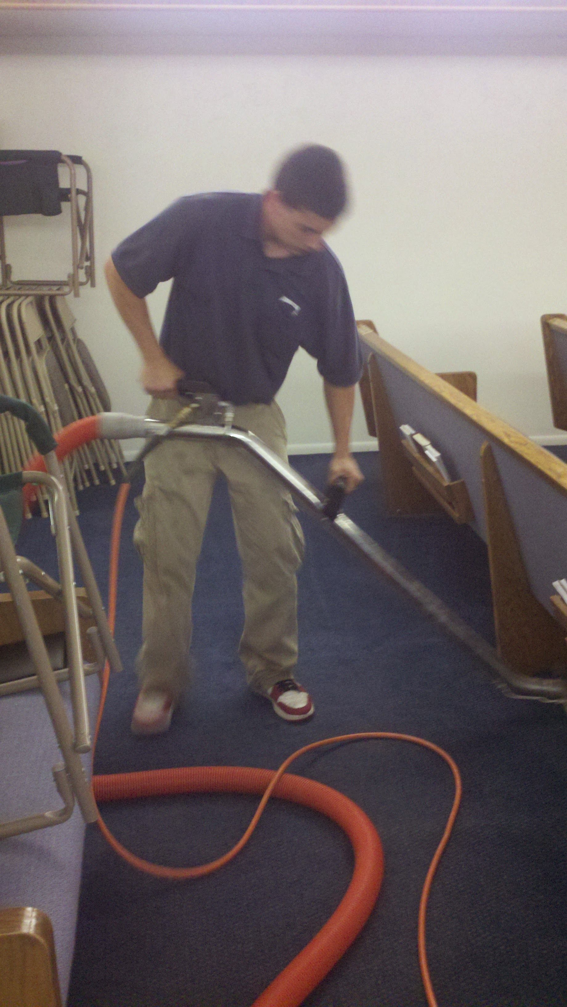 Man using a vacuum hose to clean blue carpet in a church aisle