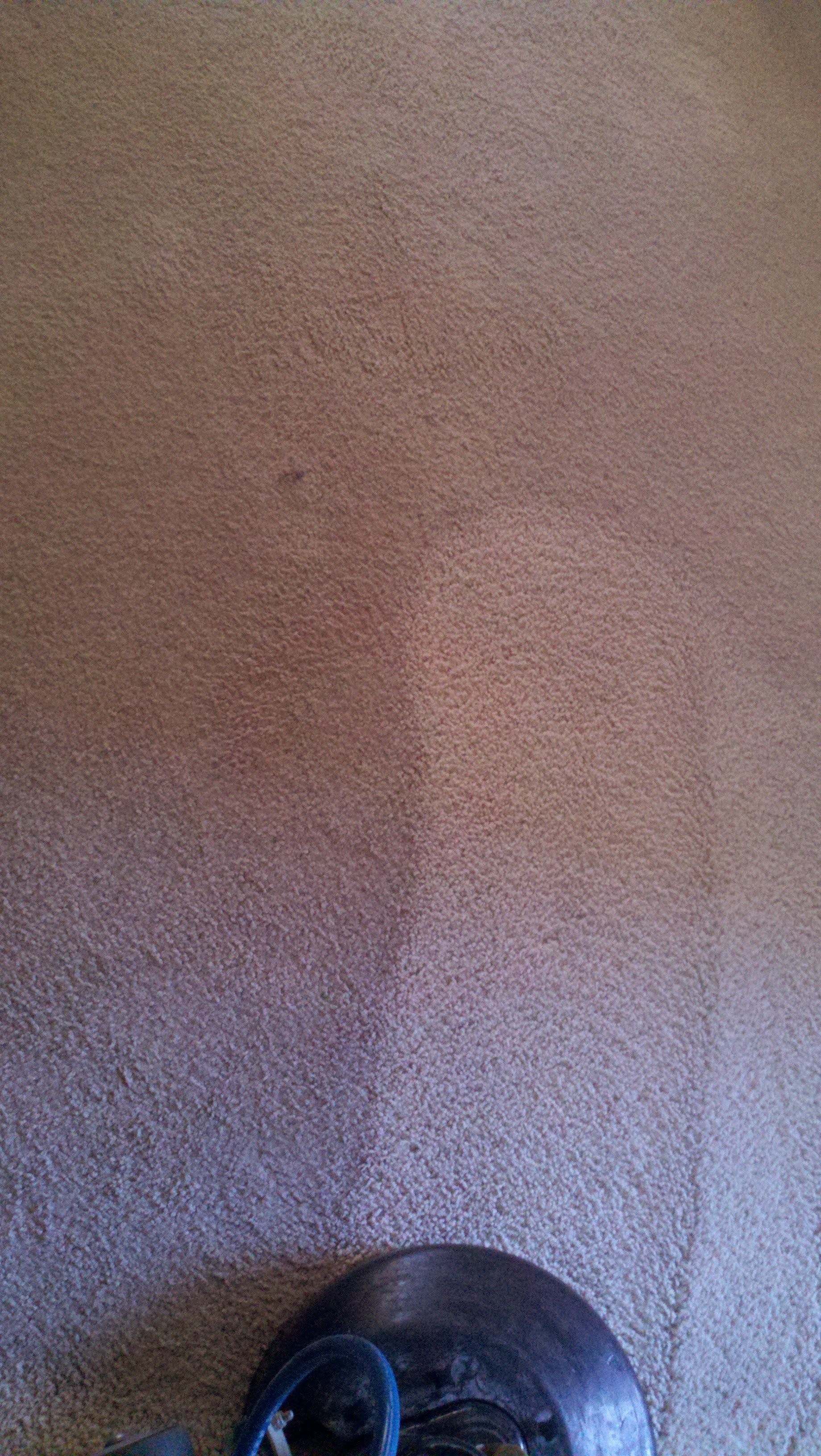Close-up of a beige textured wall with a faint vertical shadow and a small blue object at the bottom edge