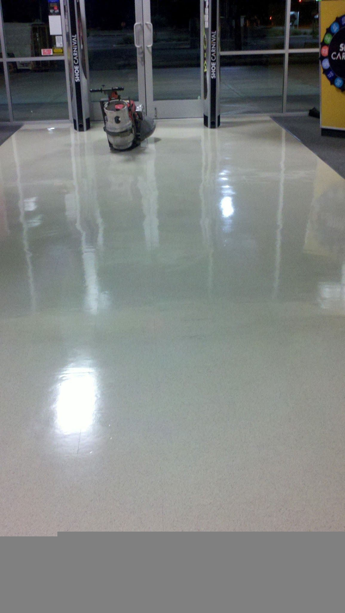 Empty store entrance with a small robot vacuum on a glossy floor near the doors.