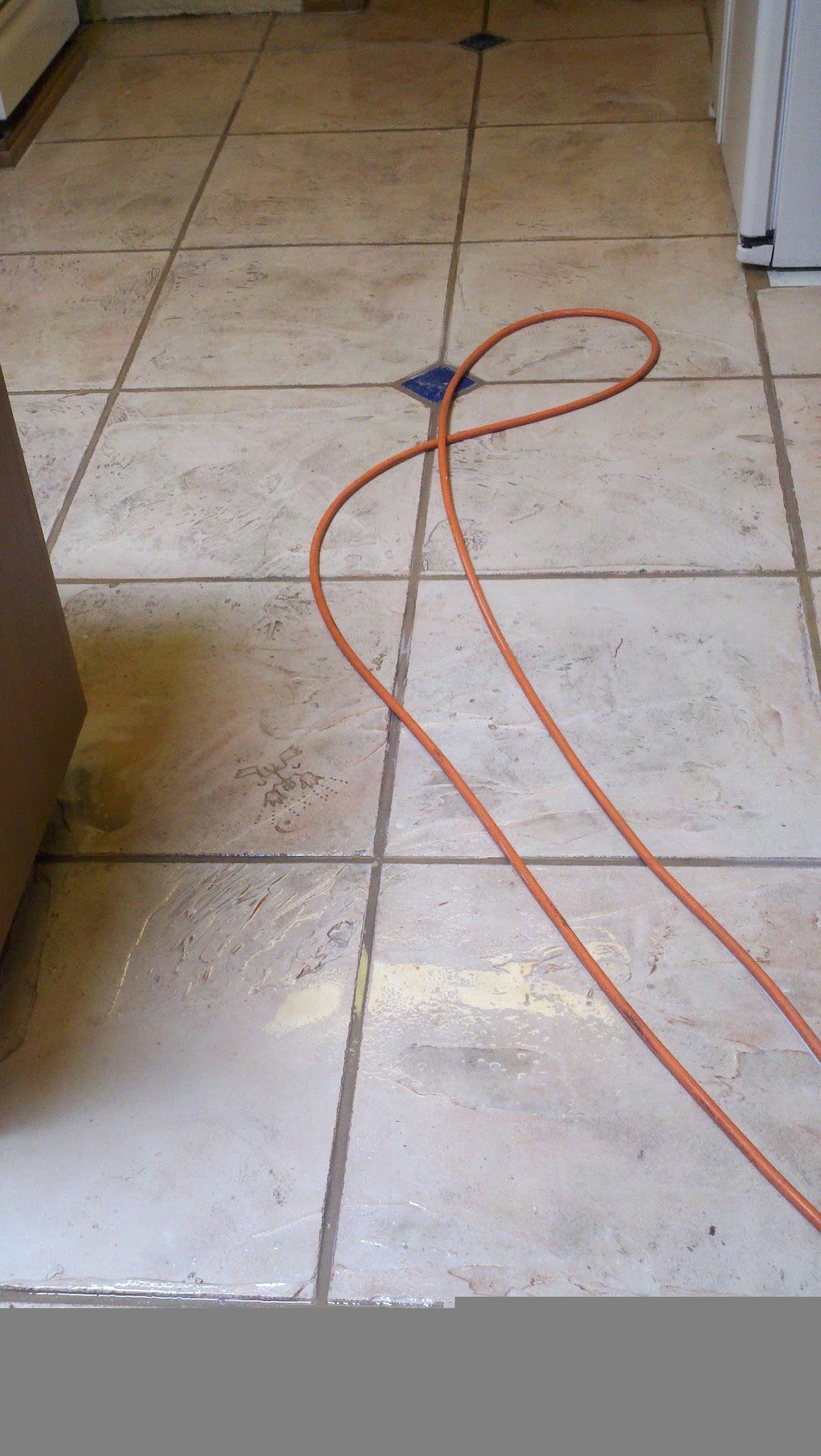 Orange extension cord looped across a tiled floor near a wall and doorway.