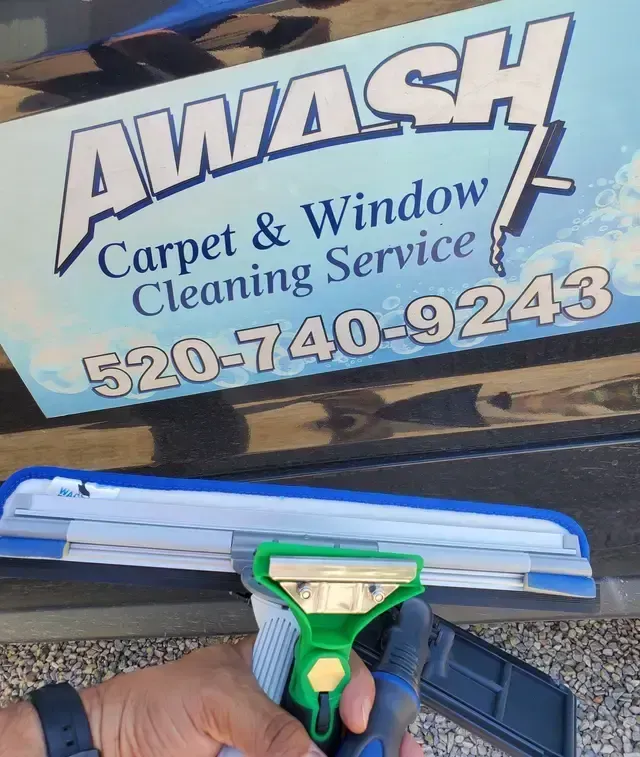 Hand-held window squeegee cleaning a truck sign for AWASH Carpet & Window Cleaning Service.