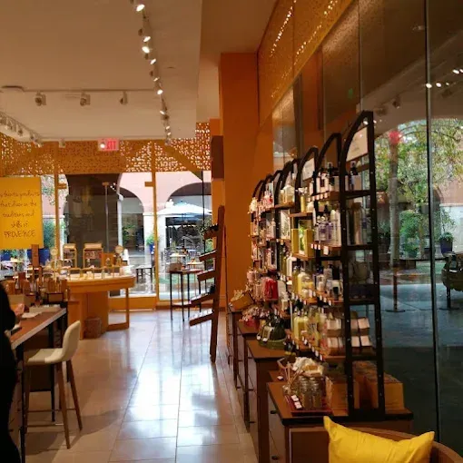 Warm café interior with wooden tables, hanging lights, and display shelves by a glass wall.