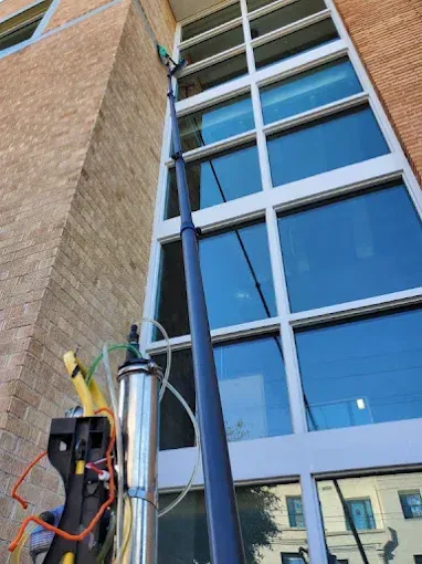 Worker in orange safety gear rappelling down a glass office building facade