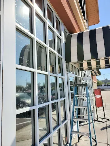 Person cleaning tall windows in a modern office lobby while another mops the floor.
