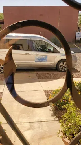 White van parked outside a building, seen through a circular metal sculpture in the foreground.