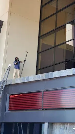 Worker on a ladder adjusting a camera or microphone on the side of a tall building.