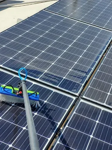 Roof solar panels being cleaned with a long-handled brush and water hose