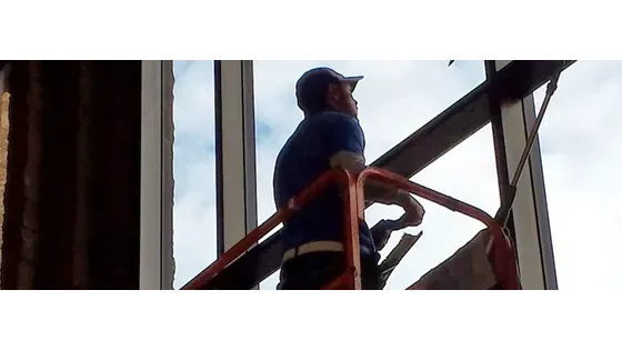 Worker on an orange lift inspecting a window in a building interior